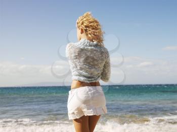 Back view of young blond woman standing at water's edge on Maui, Hawaii beach gazing at the ocean.