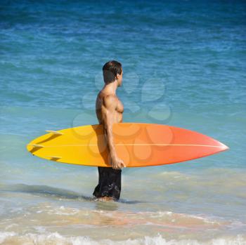 Attractive man standing in water holding surfboard in Maui, Hawaii.