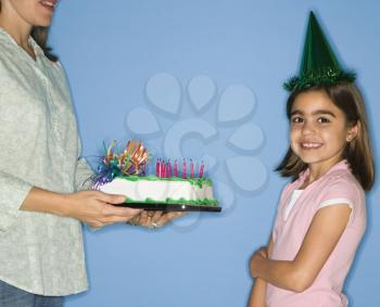 Royalty Free Photo of a Girl Wearing a Party Hat With Her Mother Holding a Birthday Cake