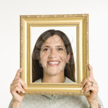 Woman holding frame in front of face smiling.