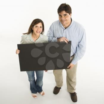 Couple standing smiling holding blank sign against white background.