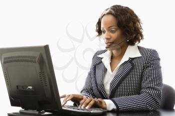 Royalty Free Photo of a Businesswoman Sitting at an Office Desk Typing on a Computer and Talking into a Headset
