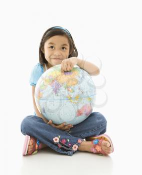 Asian girl sitting on floor holding Earth globe in her lap.