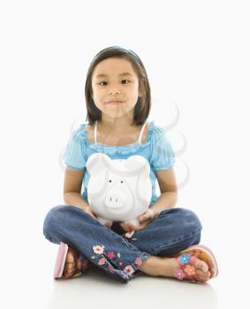 Asian girl sitting on floor holding piggybank.