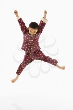Asian boy in traditional attire jumping into air excitedly against white background.