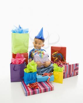 Royalty Free Photo of an Asian Boy Wearing a Party Hat Sitting With a Pile of Wrapped Presents