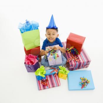 Royalty Free Photo of a Boy Sitting Smiling Wearing a Party Hat With Wrapped Presents