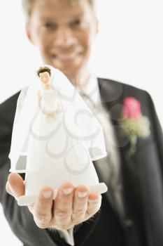 Caucasian groom holding out bride figurine in palm of his hand.
