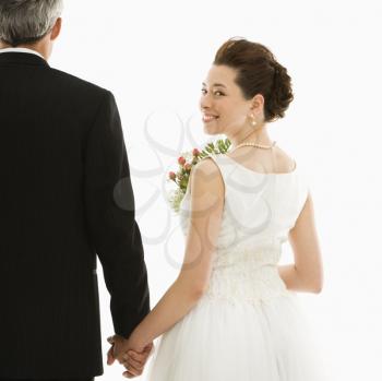 Royalty Free Photo of a Bride Looking Over Her Shoulder While Holding Her Groom's Hands