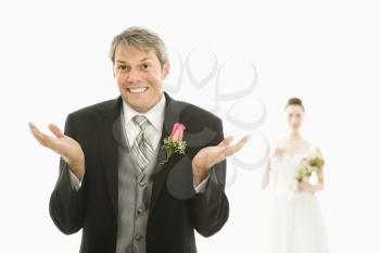 Royalty Free Photo of a Caucasian Groom in Foreground With Hands Raised in the Air and Asian Bride in the Background