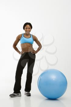 Royalty Free Photo of a Woman Smiling With Hands on Hips Standing Next to an Exercise Ball