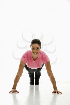 Mid adult multiethnic woman wearing pink exercise shirt doing pushups while looking at viewer and smiling.