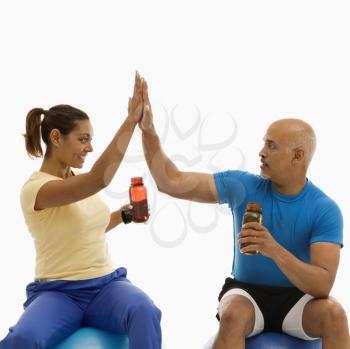 Royalty Free Photo of a Man and Woman Sitting on Exercise Balls Giving One Another a High Five