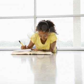 Royalty Free Photo of an African American Girl Lying on the Floor Doing Homework