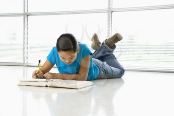 Royalty Free Photo of a Preteen Girl Lying on the Floor Doing Homework