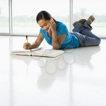 Royalty Free Photo of a Preteen Girl Lying on the Floor Doing Homework While Talking on a Cellphone