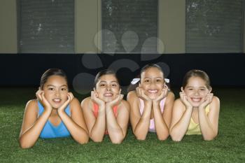 Royalty Free Photo of Four Girls Lying on the Ground in an Indoor Gym With Heads on Hands Smiling