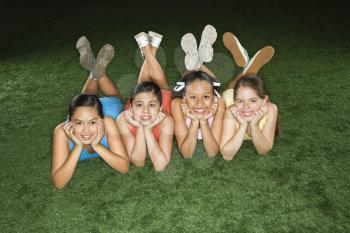 Royalty Free Photo of Four Girls Lying on the Ground in an Indoor Gym With Heads on Hands Smiling