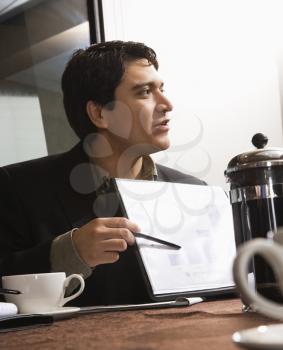 Businessman sitting at table pointing to bar graph.