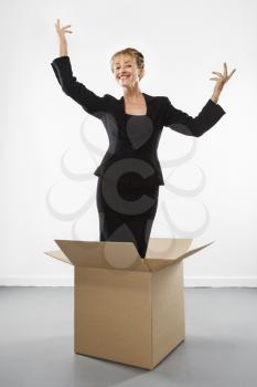 Royalty Free Photo of a Businesswoman Standing in a Cardboard Box Gesturing Above Her Head and Smiling at the Viewer