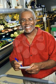 Royalty Free Photo of a Man in a Grocery Store Holding a Shopping List and Smiling