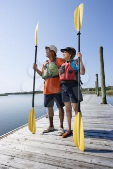 Royalty Free Photo of a Middle-aged Couple Standing on Boat Dock Holding Paddles Wearing Life Preservers