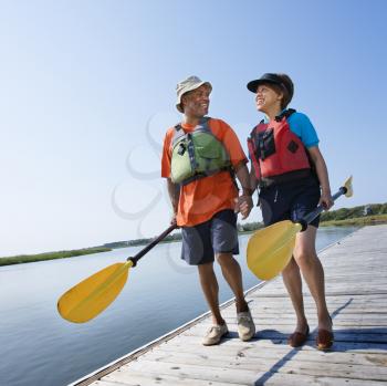 Royalty Free Photo of a Couple Walking on a Boat Dock Holding Hands and Carrying Paddles