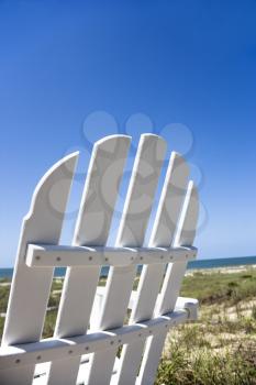 Royalty Free Photo of an Empty White Adirondack Chair Facing the Beach