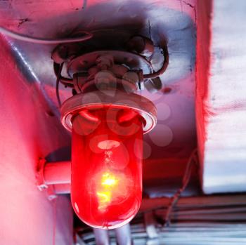 Royalty Free Photo of a Red Light Bulb Glowing From a Rustic Fixture