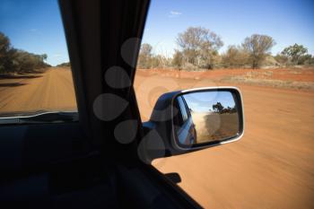 Royalty Free Photo of a Vehicle on a Dirt Road With a Rear View Mirror Reflection of Rural Australia
