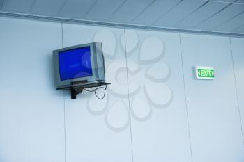 Royalty Free Photo of a Monitor Mounted to a Wall Next to an Exit Sign in an Airport