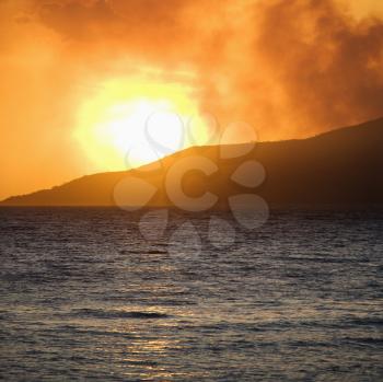 Royalty Free Photo of a Sun Setting Behind a Mountain With Ocean at Maui, Hawaii
