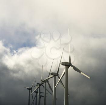 Row of turbines at wind farm again cloudy gray sky.