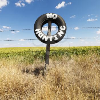 Royalty Free Photo of a Barbed Wire Fence with Tire Reading No Hunting in Front of an Agricultural Field