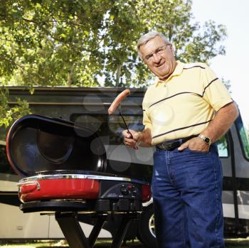 Royalty Free Photo of an Older Man Grilling Hotdogs With RV in the Background