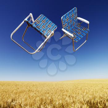 Royalty Free Photo of Two Lawn Chairs in Mid-Air Above a Field of Wheat