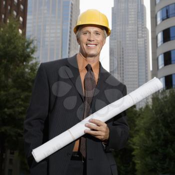 Caucasian middle aged businessman holding blueprints wearing hard hat. 