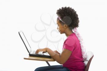 Royalty Free Photo of a Girl Sitting in a School Desk Typing on a Laptop