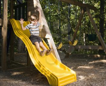 Royalty Free Photo of a Boy Sliding Down an Outdoor Slide With Arms Raised Above Head