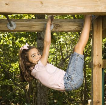 Royalty Free Photo of a Girl Hanging by Arms and Legs From Monkey Bars