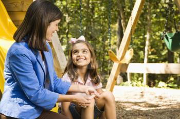 Royalty Free Photo of a Girl Sitting on a Playground Slide Smiling at a Woman Applying a Bandage to Her Knee