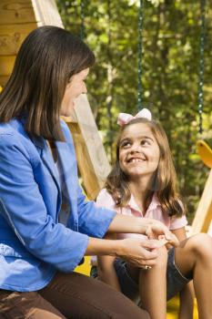 Royalty Free Photo of a Girl Sitting on a Playground Slide Smiling at a Woman Applying a Bandage to Her Knee