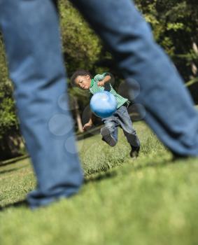 Royalty Free Photo of a Son Running and Kicking a Ball Towards His Father in a Park