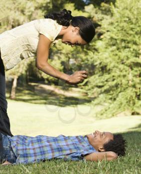 Royalty Free Photo of a Woman Standing Over a Smiling Man Lying in Grass Taking His Photograph