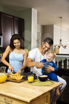 Caucasian family with toddler in kitchen at breakfast.