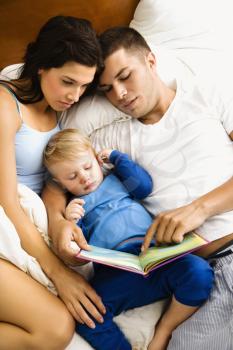 Royalty Free Photo of Caucasian Parents Reading to Their Toddler Son in Bed
