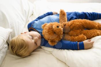 Caucasian toddler boy sleeping in bed with teddy bear.