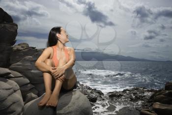Royalty Free Photo of a Woman Sitting on a Rock Looking Over Her Shoulder Smiling in Maui, Hawaii