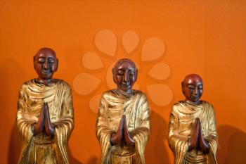 Royalty Free Photo of Three Wooden Statues of Buddhist Disciples Against an Orange Wall
