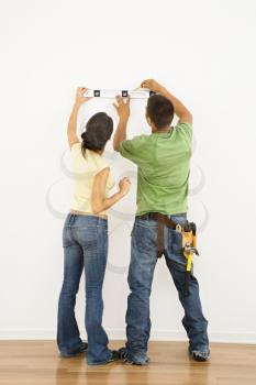 Couple holding level to interior wall and marking with pencil.